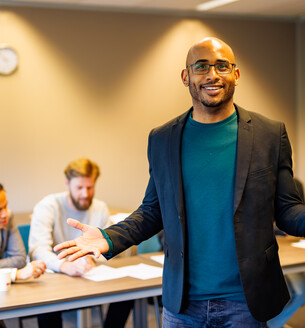 Docent in lokaal gebaart naar de camera