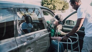 Persoon met looprek wordt uit auto geholpen