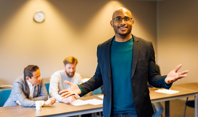 Docent in lokaal gebaart naar de camera